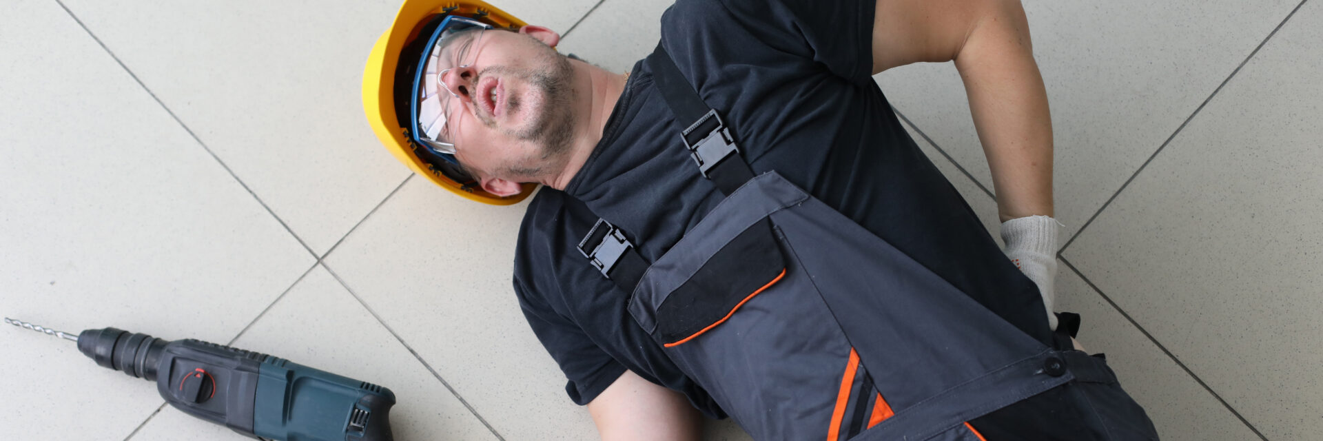 Portrait of man lying at floor with drill in hands. Handyman fell off ladder holding back. Incident at work. Dangerous profession of person with backache and pains in spine